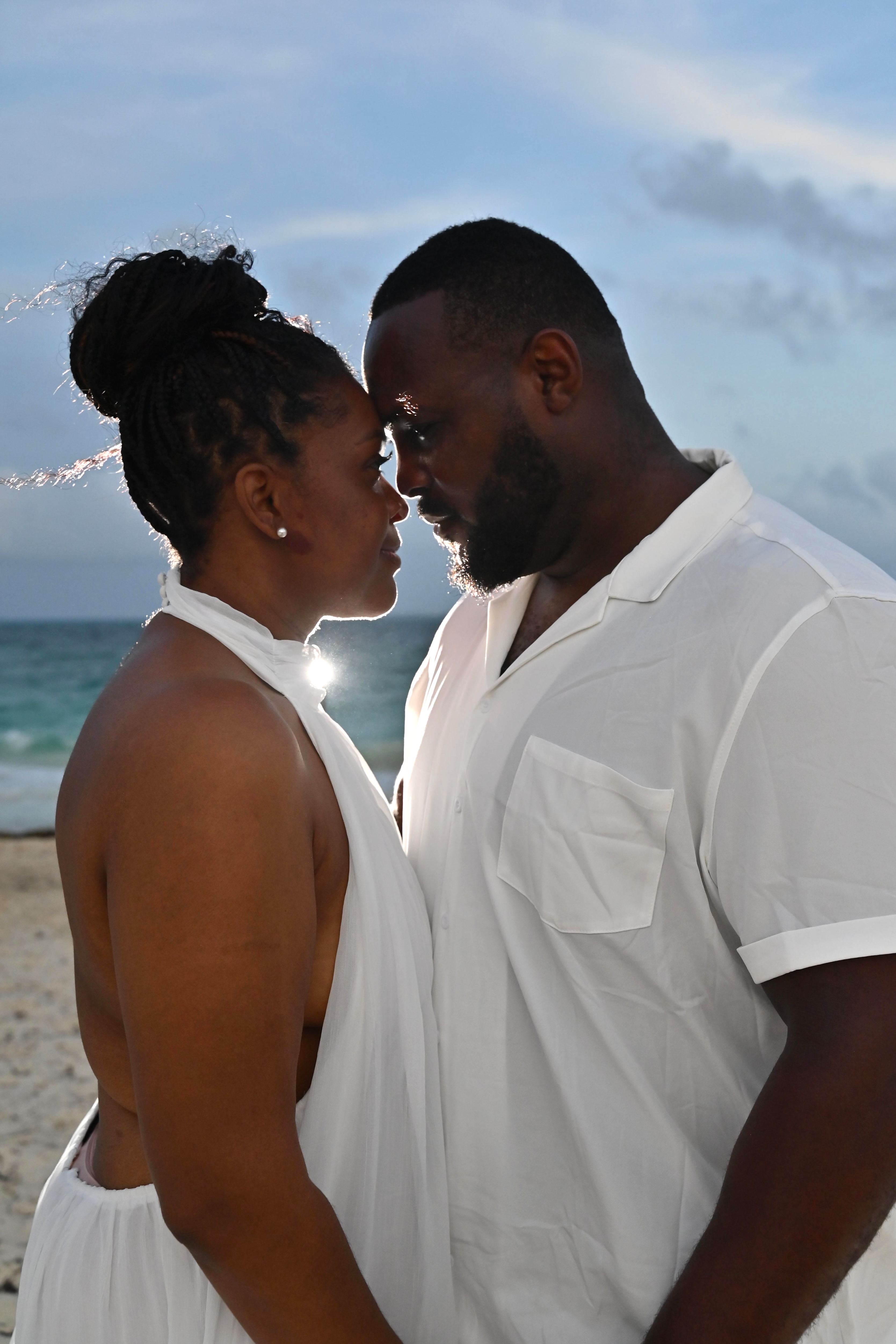 Couple holding hands on a beach as one kisses the other's forehead